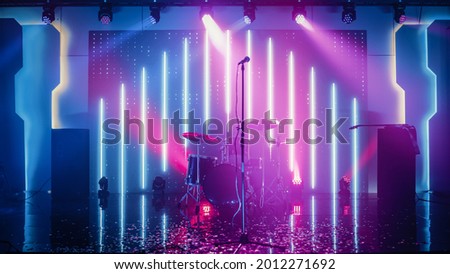 Empty Concert Stage in a Night Club. Professional Drum Kit and Other Music Equipment for Live Gig with Rock Band. Confetti on the Dance Floor. Bright Colorful Strobing Lights on Stage. Royalty-Free Stock Photo #2012271692
