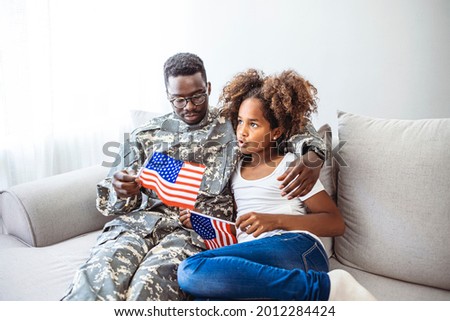 Portrait of happy american family father in military uniform and cute little girl daughter with flag of United States hugging and smiling at camera, male soldier dad reunited with family at home