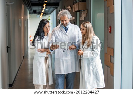 Man and women doctor having a discussion in hospital hallway while holding digital tablet. Doctor discussing patient case status with his medical staff after operation. 