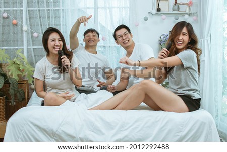 Group of four Asian friends wearing casual clothes, having party with fun and happiness, singing and dancing together on bed in bedroom at comfortable home during the holidays. Lifestyle Concept
