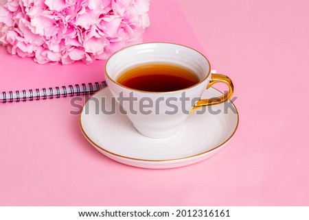 Cup of tea, notebook and hydrangea with copy space on pink background