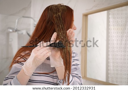 Young woman dyeing her hair with henna near mirror indoors