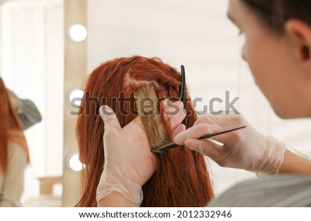 Professional hairdresser dyeing woman's hair with henna in beauty salon, closeup