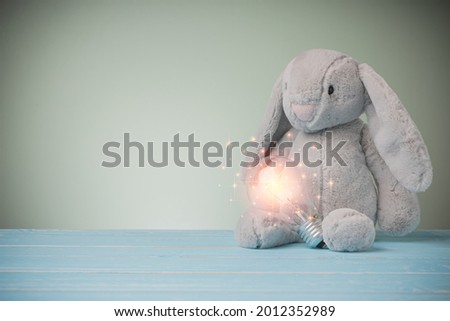 Cute doll bunny animal and fluffy fur for kids, baby. Rabbit doll big ears with a light bulb on blue wooden table with copy space. idea concept with innovation and inspiration.