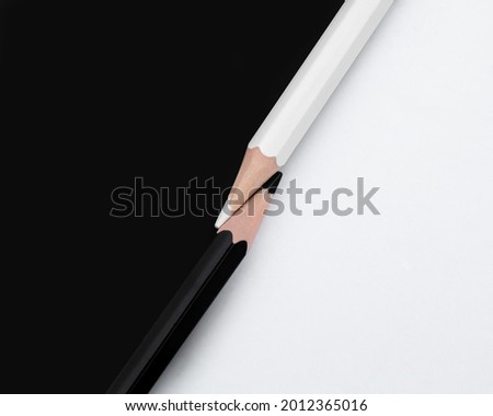 Macro shot of two black and white colored pencils with the tips touching on a matching background with opposite colors. Top down view flat lay. Concept of contrast or opposites attract Royalty-Free Stock Photo #2012365016