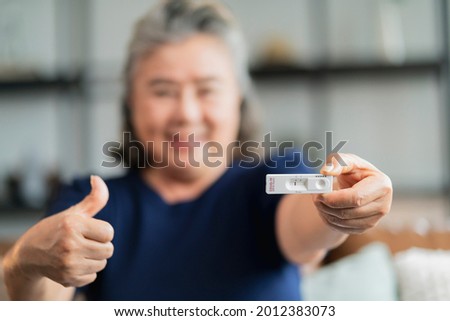 old senior retired asian female hand hold gesture and show covid-19 rapid test kit result with negative sign with happiness and cheerful,self test rapid test at home 
