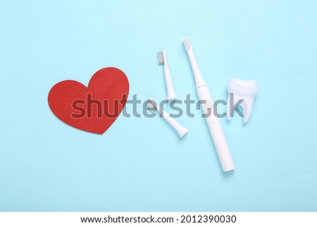 Ultrasonic plastic toothbrush with replaceable heads, heart and tooth model on a blue background. Dental care concept. Top view