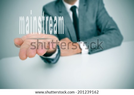 man wearing a suit sitting in a desk holding the word mainstream in his hands