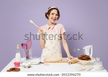 Young fun smiling happy housewife housekeeper cook chef baker woman in pink apron work at table kitchenware hold wooden spoon isolated on pastel violet background studio Process cooking food concept Royalty-Free Stock Photo #2012396270
