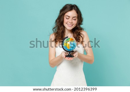 Smiling pretty bride young woman 20s years old in beautiful white wedding dress hold Earth world globe isolated on blue turquoise color background studio portrait. Ceremony celebration party concept
