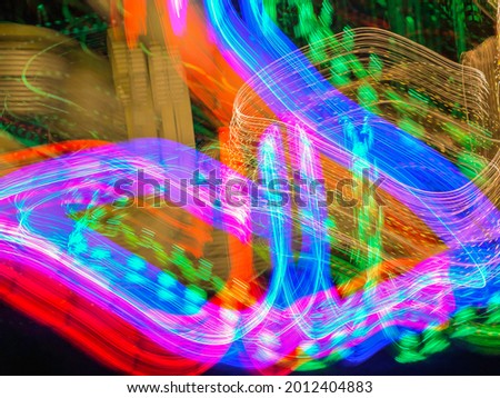 Broad and narrow light trails of luminous holiday LED display in a suburban front yard at night. Long exposure with motion blur. Light painting.