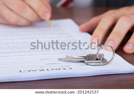 Cropped image of man signing contract with keys on it