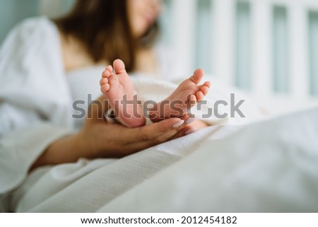Baby feet in parent hands. Mother and her child. Seet small feet of newborn baby. Mom and baby at white bedroom on the bed. Beautiful conceptual image of Maternity. Royalty-Free Stock Photo #2012454182