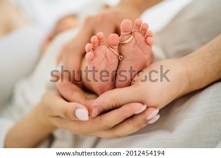 Closeup of parents hands holding newborn baby feet with wedding rings. Relation, love, childbirth and new family. Royalty-Free Stock Photo #2012454194
