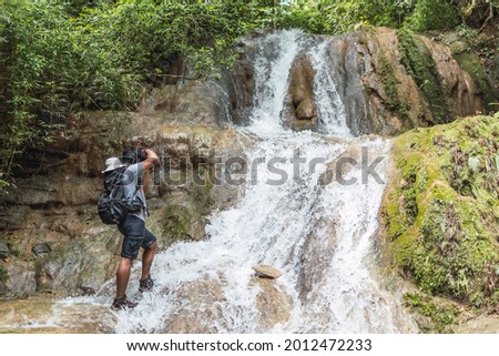 Young man taking photos with camera in waterfall in river in mountain