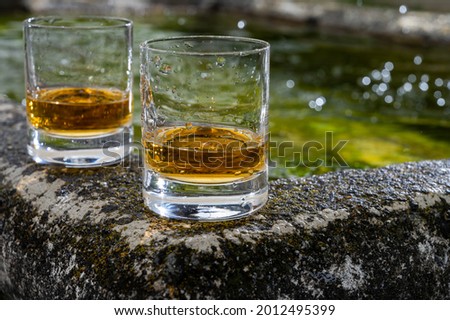 Glasses of strong scotch single malt whisky served on old stone reservoir for water from mountain spring, Scotland