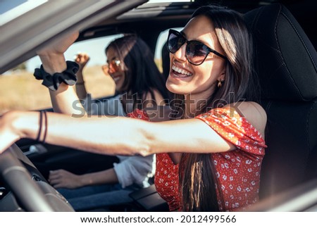 Shot of pretty young women singing while driving a car on road trip on beautiful summer day. Royalty-Free Stock Photo #2012499566