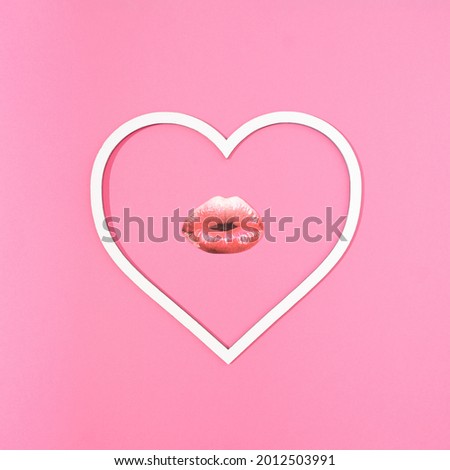 Women's lips with red lipstick in a white heart shaped frame on a pink background. Romantic love minimal creative concept.