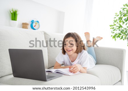Photo portrait little girl laying on couch watch online lesson laughing keeping pen