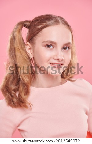 Portrait of a pretty teenage girl in light summer clothes and with funny ponytails smiling at camera. Teenage style. 