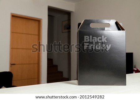 Black Friday gift box on the table with black packaging with writing in dark gray and living room in the background. Black friday concept. Gift concept. Copy space.
