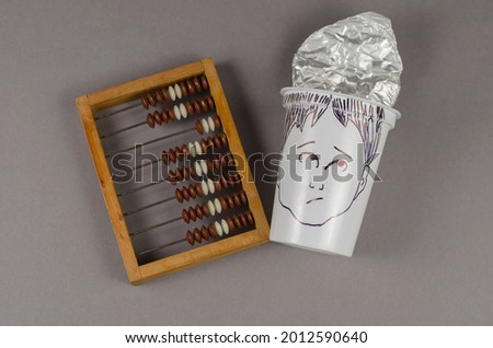 An old wooden abacus and a surprisingly human face painted on the plastic cup. White empty cup with a foil lid. Business concept, accounting, calculations.