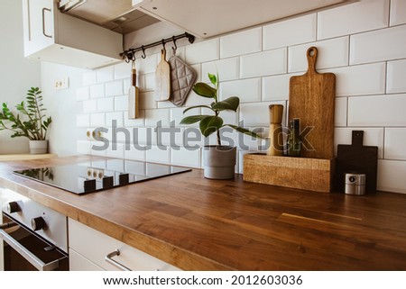 Kitchen brass utensils, chef accessories. Hanging kitchen with white tiles wall and wood tabletop.Green plant on kitchen background side view