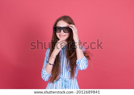 Little kid girl 13 years old in blue dress with brackets isolated on pink background wearing 3d cinema glasses happy smiling laugh