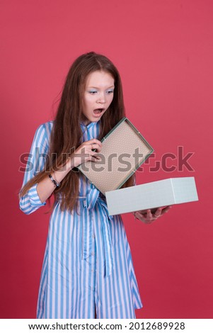 Little kid girl 13 years old in blue dress isolated on pink background opening gift box  shocked open mouth