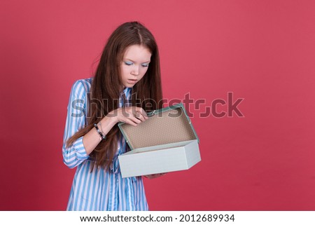 Little kid girl 13 years old in blue dress isolated on pink background holding gift box shocked with open mouth