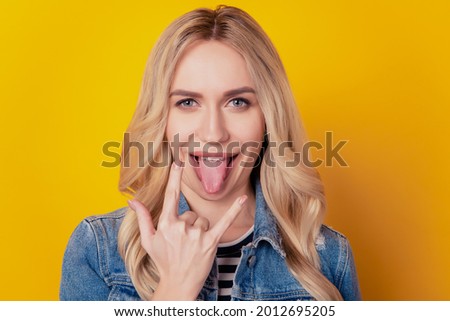 Portrait of funky positive rock fan girl showing horns sign protrude tongue on yellow background