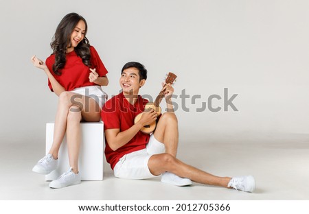 Young attractive Asian couple wearing red t shirt and white shorts sitting. man playing ukulele against white background. Concept for pre wedding photography. Isolated. Royalty-Free Stock Photo #2012705366