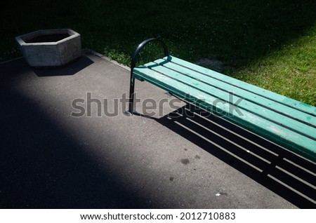 A bench in a city park, which is in the light around the darkness of shadows. Copy space.