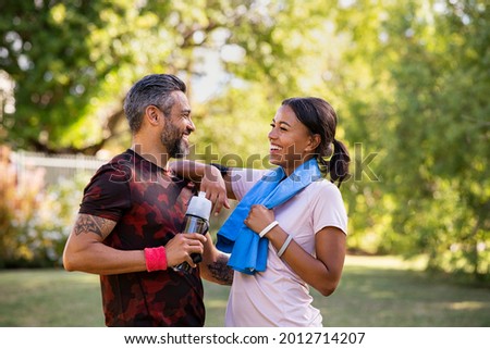Cheerful multiethnic couple resting together after jogging in the park. Happy mature man and beautiful woman laughing while resting after running. Woman and indian man taking a break after fitness. Royalty-Free Stock Photo #2012714207