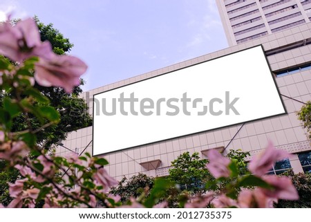 Blank advertising poster banner mockup on building exterior, flowers plants in foreground; large digital lightbox display screen. Billboard poster, out-of-home OOH media display space