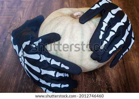 Halloween decoration on a wooden background. Skeleton gloves hold a pumpkin