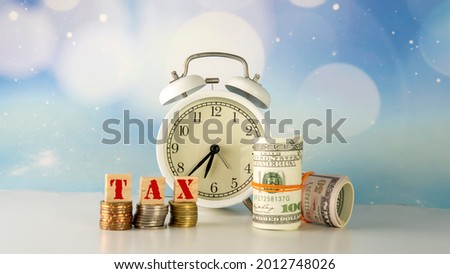 Financial concept, money, coin and clock with selective focus on tax wording isolated on blue blurred background. 