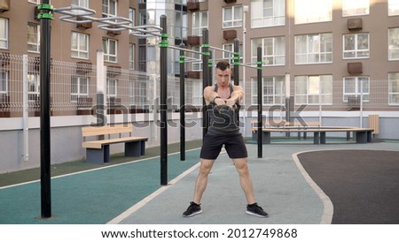 A young man lunges with kettlebells. A man lifts a kettlebell while standing in the yard. Bodybuilder doing exercises with kettlebells in the fresh air.