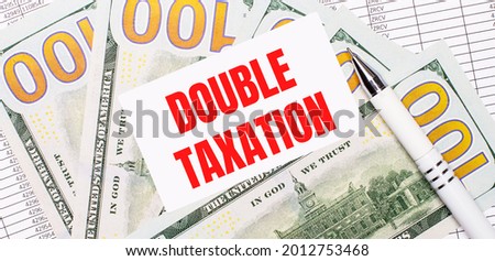 Against the background of reports and dollars - a white pen and a card with the text DOUBLE TAXATION. Business concept