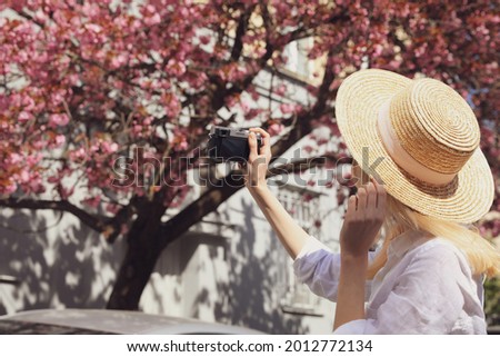 Female tourist taking photo of blossoming tree on city street