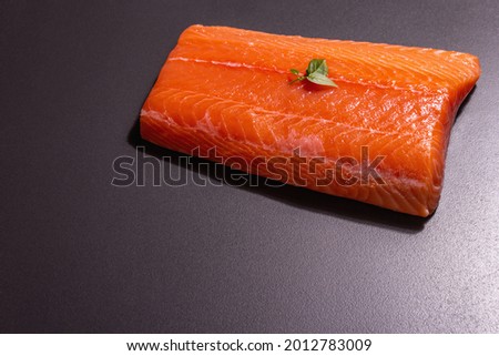 Fresh raw salmon or trout sea fish fillet on black stone background. Useful ingredient for healthy food, source of Omega 3. A modern hard light, dark shadow, culinary wallpaper, copy space