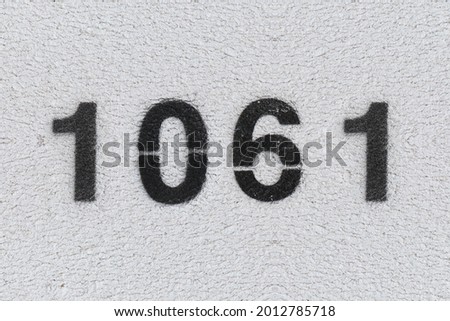 Black Number 1061 on the white wall. Spray paint. Number one thousand sixty one.