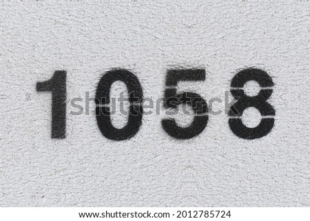 Black Number 1058 on the white wall. Spray paint. Number one thousand fifty eight.