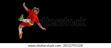 Football training. One little male football soccer player, boy training with football ball isolated on dark studio background. Concept of sport, movement, energy and dynamic. Copy space for ad. Flyer