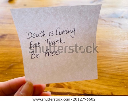 Death is coming. Eat trash. Be free. Handwritten message. Wooden background.