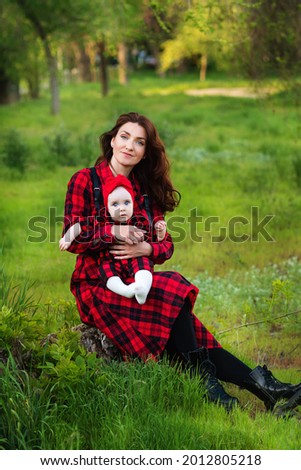 Full-length portrait good-looking young mom holding adorable toddler girl in his arms during a walk. Family look outdoor in summer. Motherhood or mother's day concept