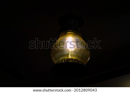  A very very dim light  lamp or bulb hanging from the ceiling of a house. This picture is taken in very low light  condition with intentional noise and grains. 