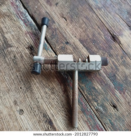 picture of a tool called a chain cutter or chain splitter placed on a wooden table meja