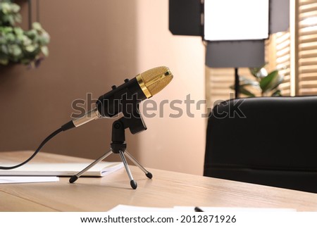 Tripod with modern microphone on wooden table in room. Blogger's workplace