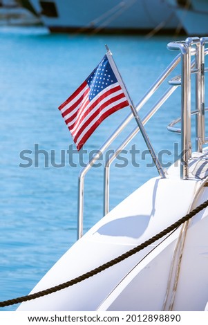 The flag of the United States flutters in the wind on a stainless steel flagpole at the stern of a motor yacht. Marina in the port city in beautiful summer sunny weather. Royalty-Free Stock Photo #2012898890
